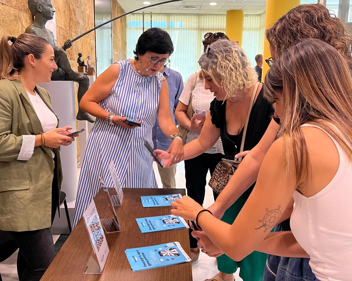 Varias personas se inscriben con su móvil en una mesa con folletos y códigos QR de una activación, acompañadas por el equipo.